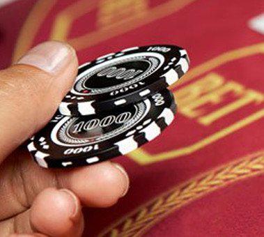 Hand holding two roulette chips over colored Baccarat table